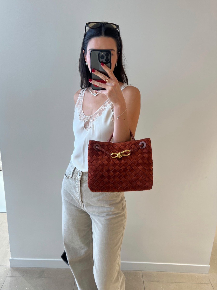 A woman photographed in a mirror holding a woven suede tote in rust brown