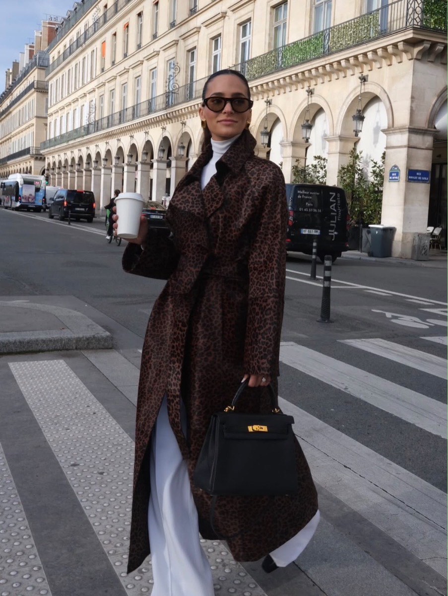 A woman crossing a Paris street in a leopard-print trench, carrying a black top-handle bag