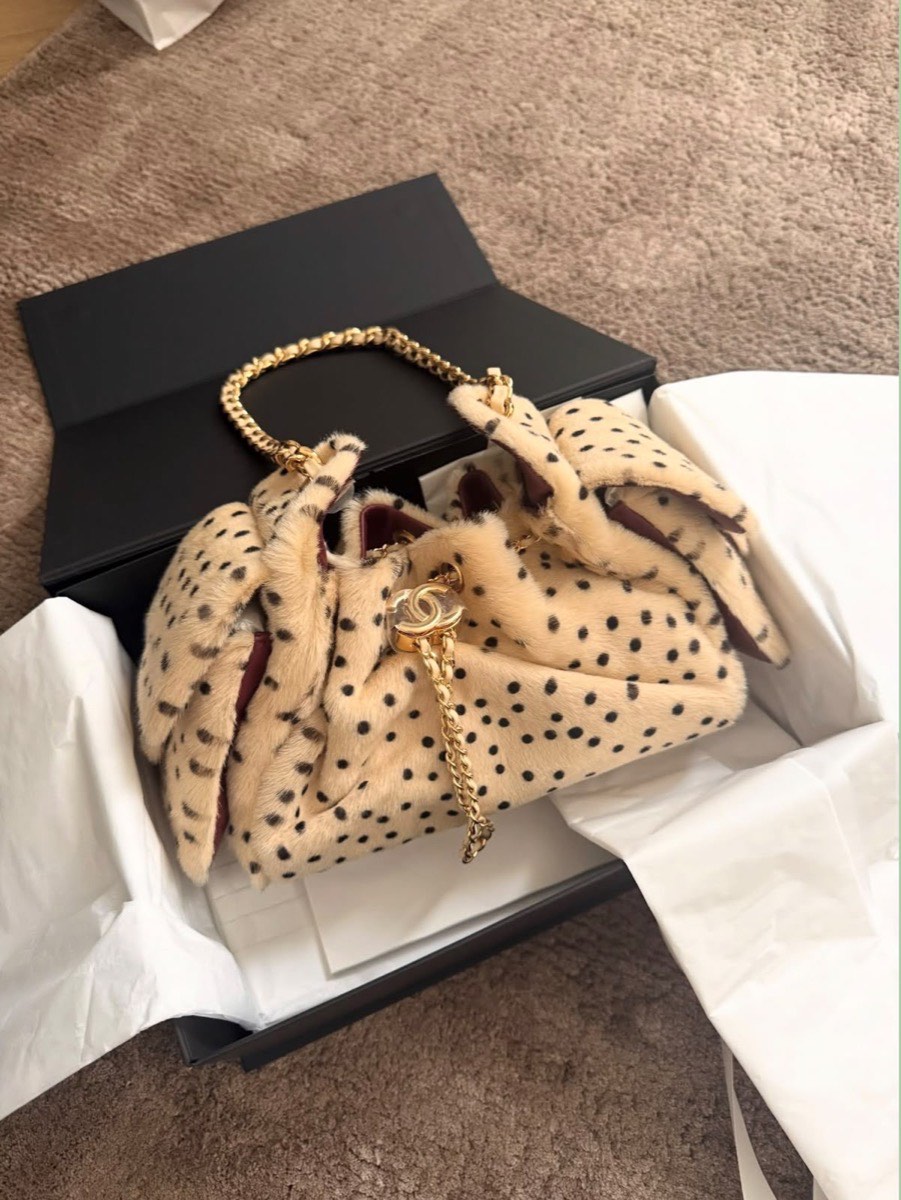 A spotted shearling Chanel bag with a gold chain, resting in its opened box